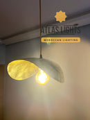 Pendant light with a textured design, glowing softly against a neutral background, branded 'Atlas Lights'.